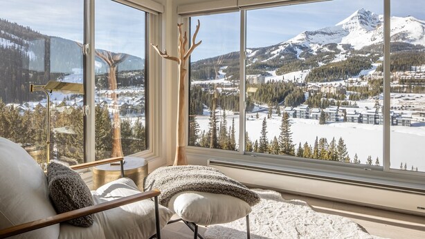 A room with a large window offering a view of a snowy mountain landscape.