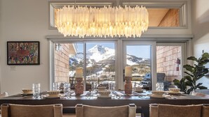 A dining area with a view of snow-capped mountains, a chandelier, and a table set with plates and glasses.