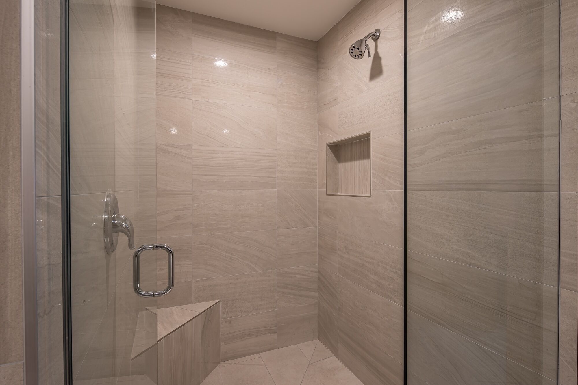 A modern shower area with a glass door, a handheld showerhead, and a small shelf.
