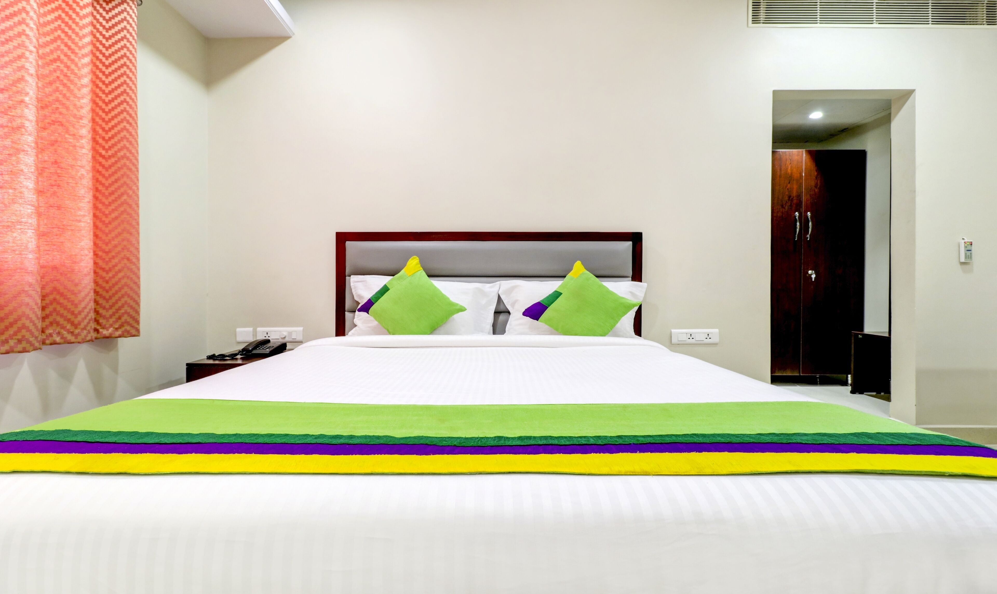 A hotel room with a bed, a nightstand, a telephone, and a door leading to another room.