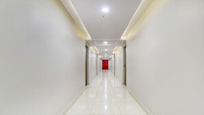 A long, narrow hallway with white walls and a red door at the end. - Treebo Grand Milan (Visakhapatnam)