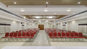 A conference room with rows of red chairs, a wooden door at the front, and white walls with patterned curtains. - Treebo Grand Milan (Visakhapatnam)