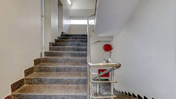 A staircase with granite steps and metal railings, leading to a landing with a red fire alarm.