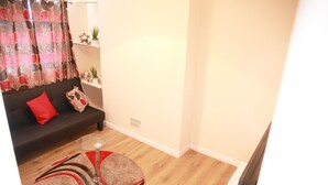 A living room with a sofa, a glass coffee table, a rug, and a curtain. - Canning Town Cozy one Bedroom Apartment (London)
