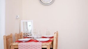 A dining area with a wooden table set for four, including plates, glasses, and cutlery. A wall-mounted clock is above the table. - Canning Town Cozy one Bedroom Apartment (London)