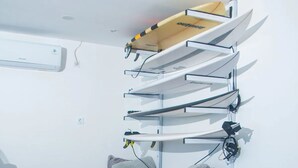 Una habitación con un sofá de madera, cojines grises y un soporte de pared para tablas de surf con varias tablas.