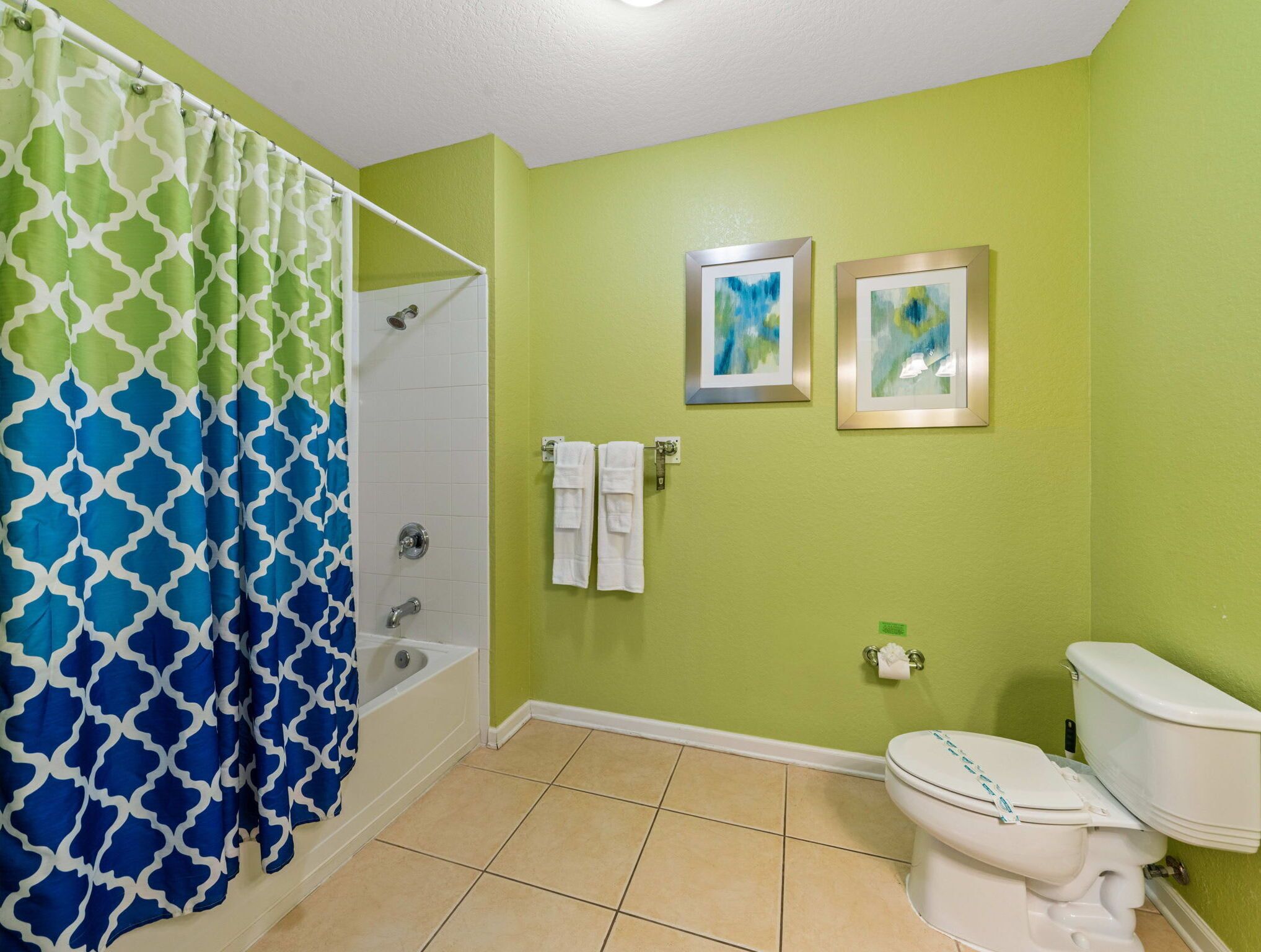 A bathroom with a shower, toilet, and two framed artworks on the wall.