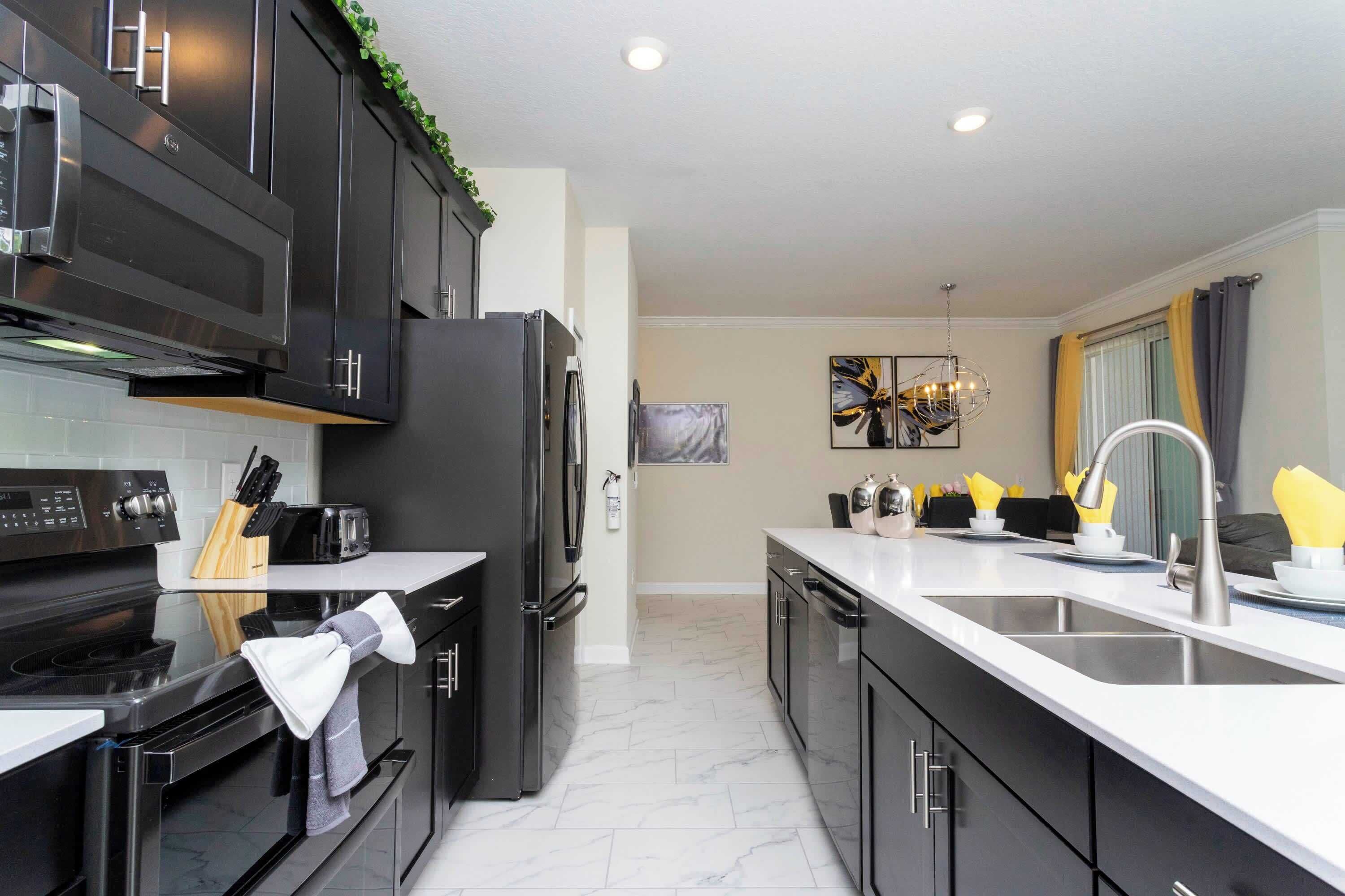 A modern kitchen with black cabinets, a stainless steel refrigerator, a built-in oven, and a large island with a sink.
