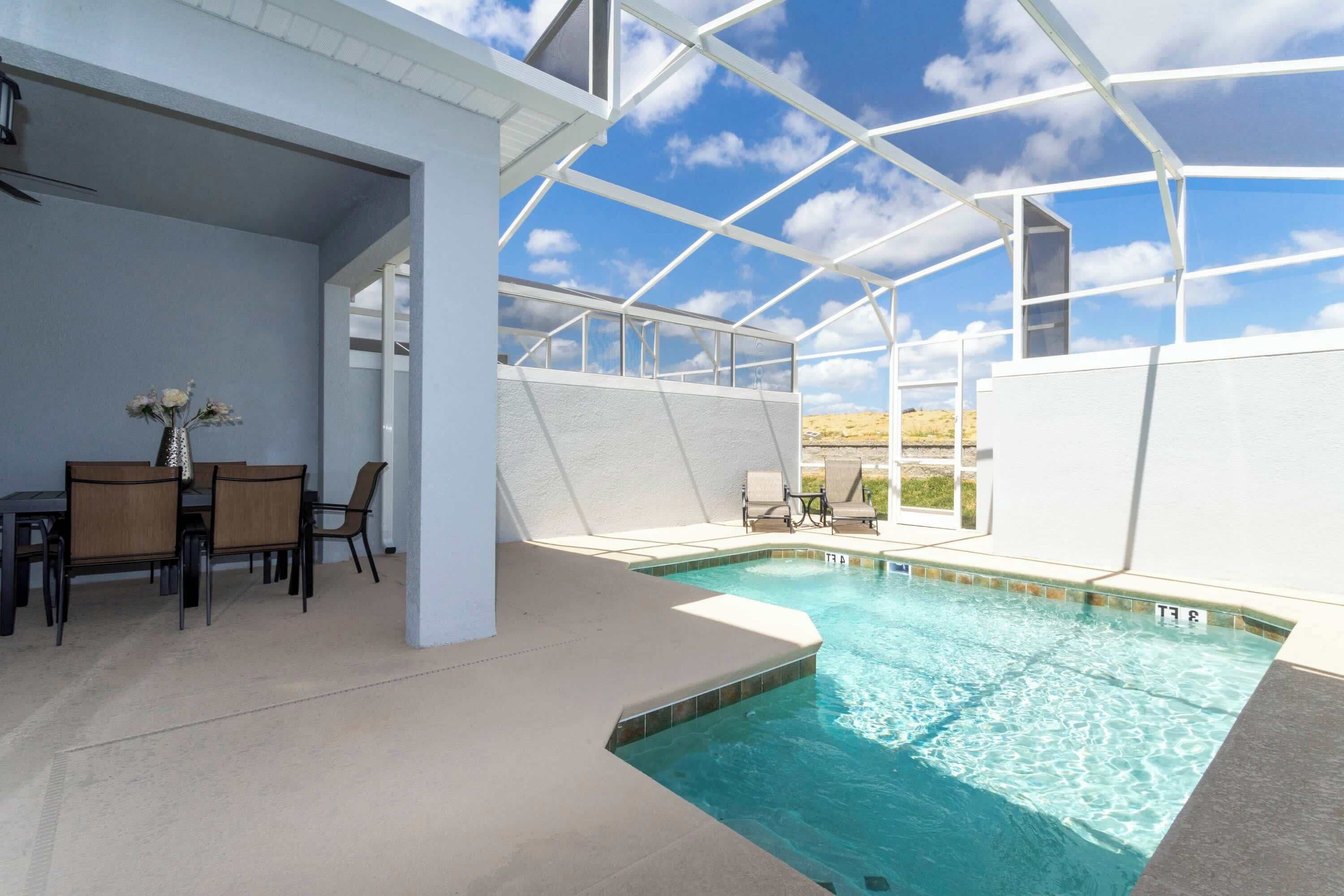 Ein Poolbereich mit Glasveranda, einem Esstisch mit Stühlen und Blick auf den Himmel.