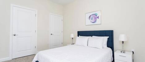Une chambre à coucher comprenant un lit, deux tables de chevet, un ventilateur de plafond et une œuvre d’art accrochée au mur.