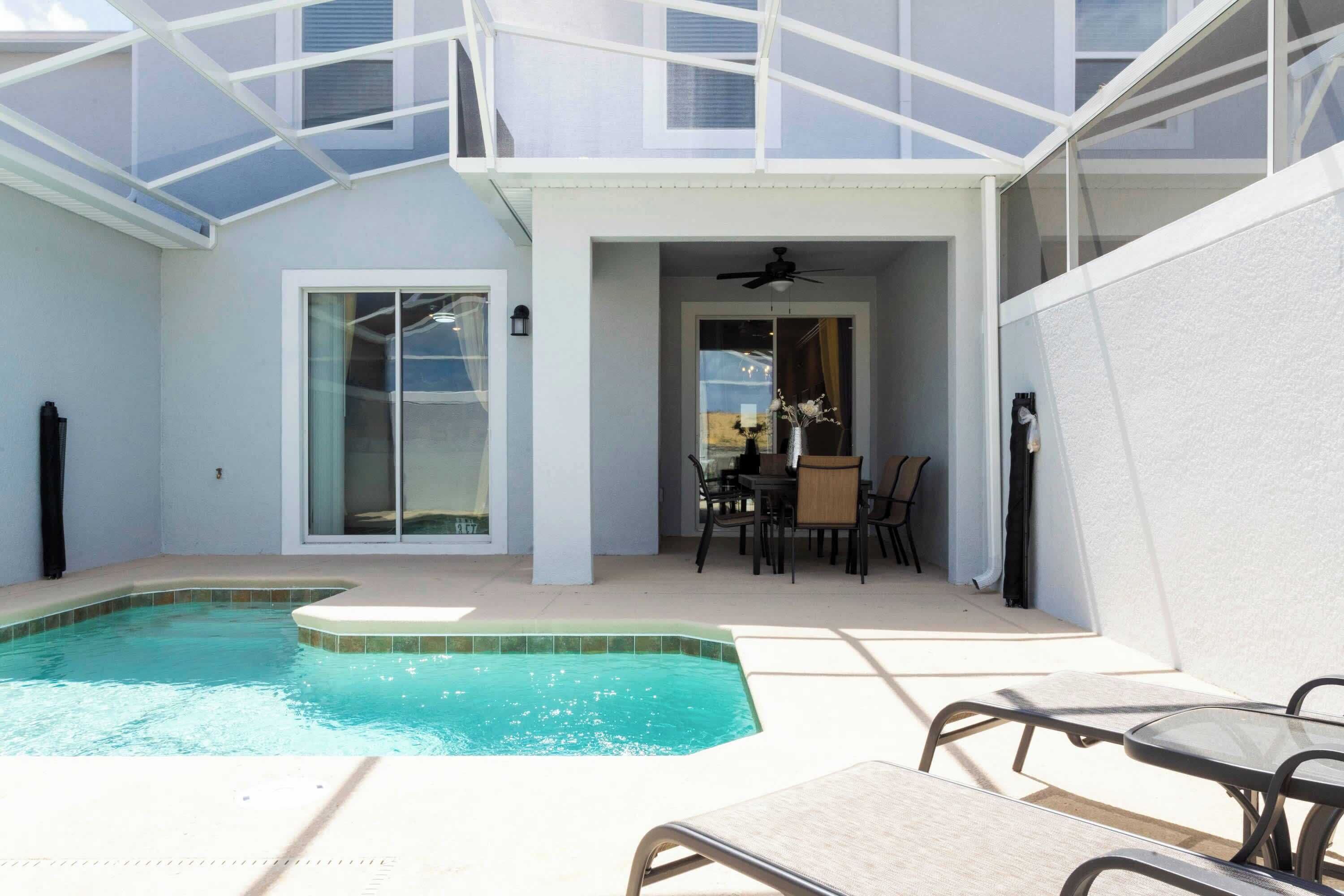 A pool area with a glass ceiling, a dining table with chairs, and a ceiling fan.