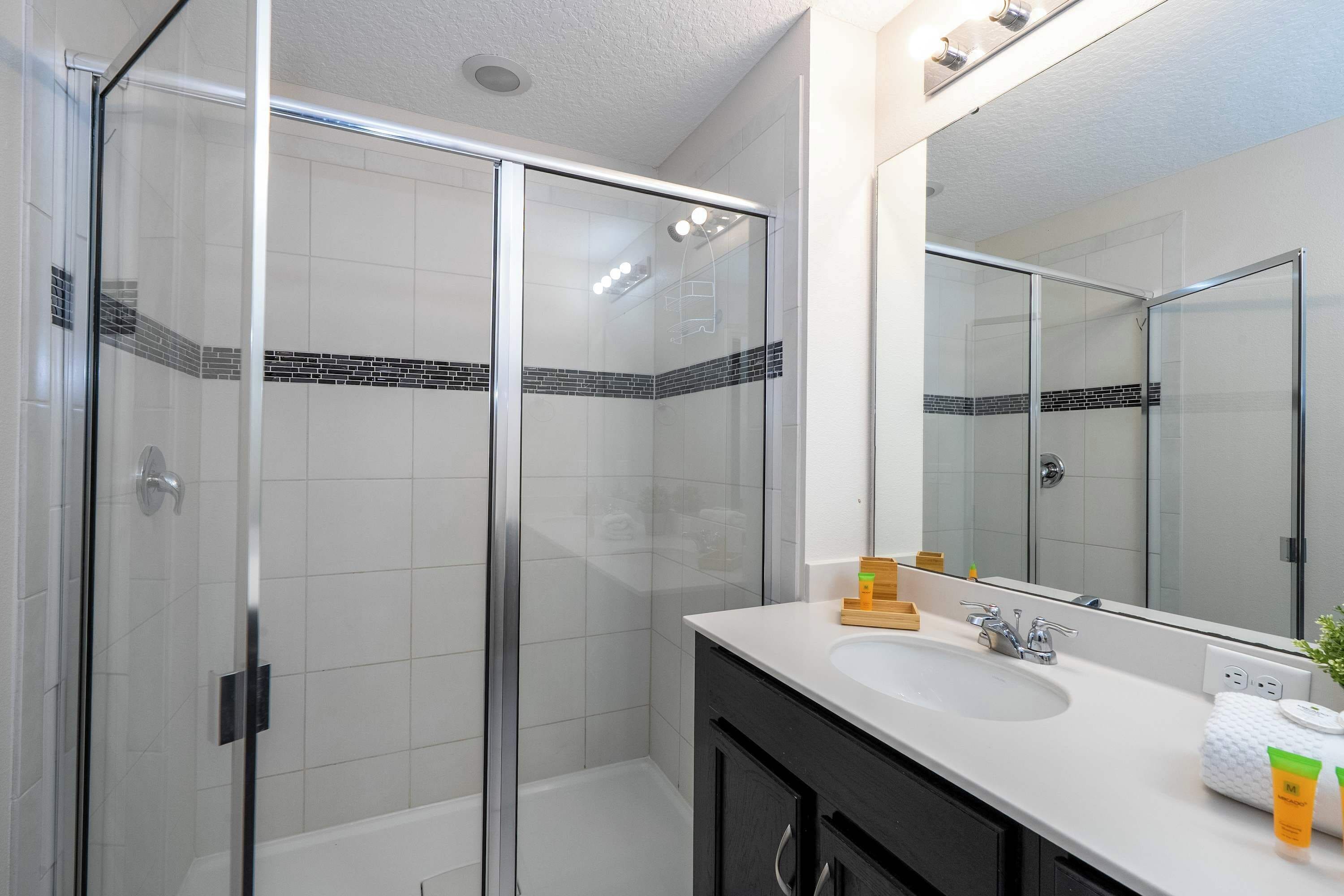 A modern bathroom with a glass-enclosed shower, a large mirror, and a white sink with toiletries.