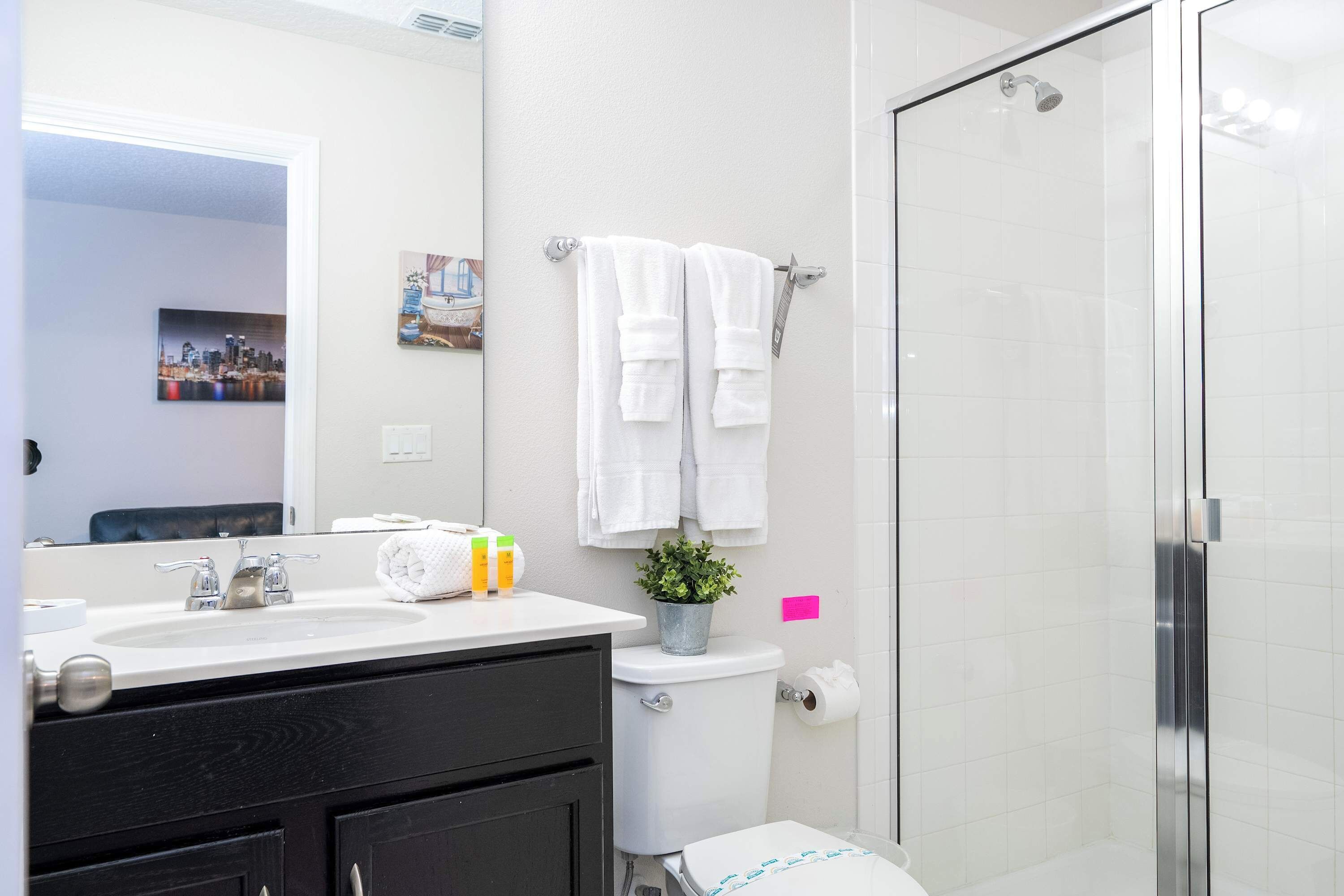 Un baño moderno con un lavamanos blanco, armarios negros, un inodoro y una cabina de ducha de vidrio.