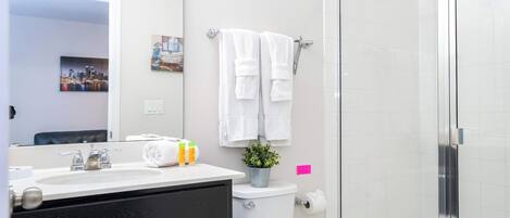 Un baño moderno con un lavamanos blanco, armarios negros, un inodoro y una cabina de ducha de vidrio.
