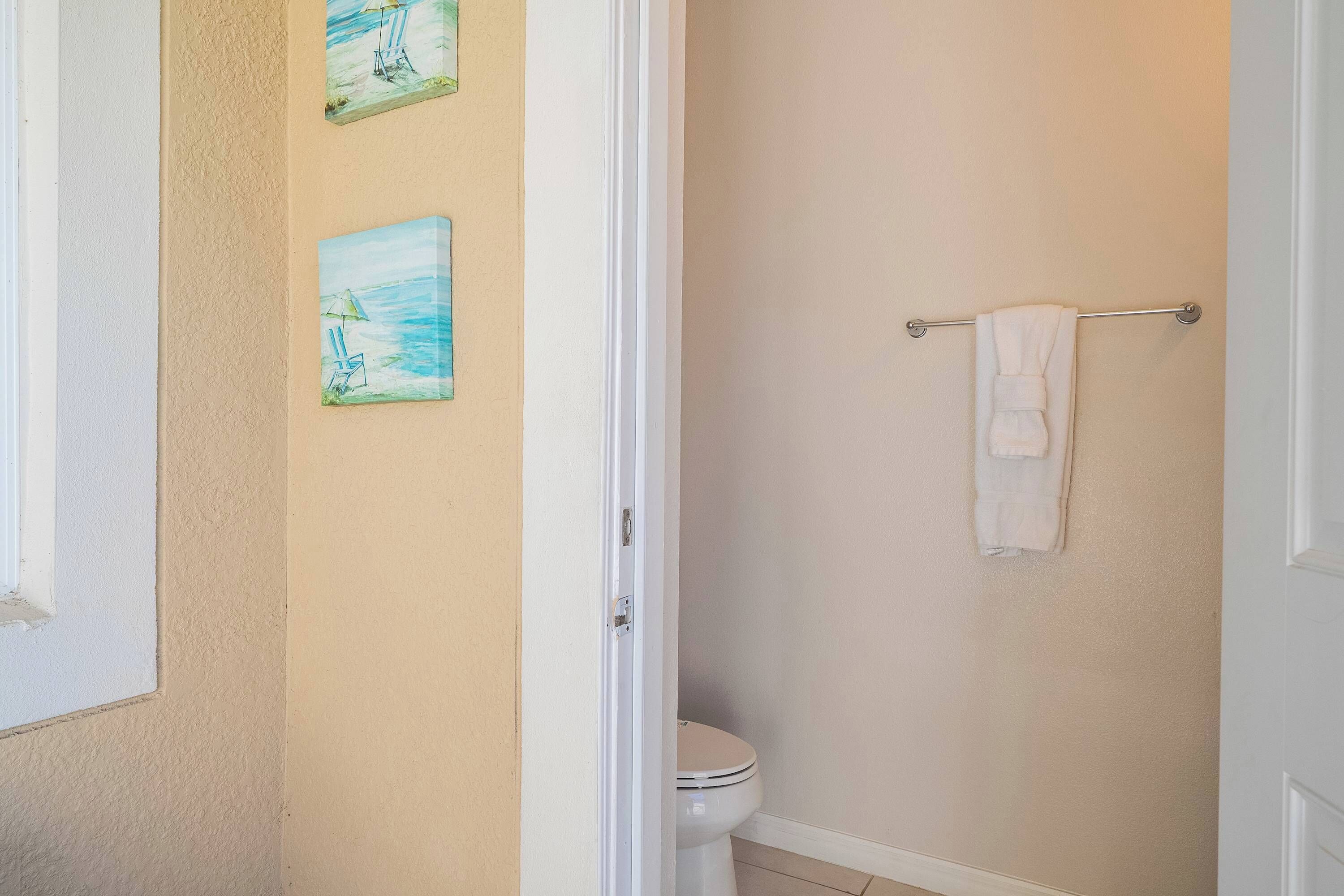 A bathroom with a toilet, a towel rack, and two wall-mounted paintings.