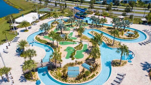 An aerial view of a resort with a large swimming pool, palm trees, and a water slide.