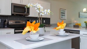 A modern kitchen with white cabinets, a microwave, and a coffee station with white cups and orange flowers.