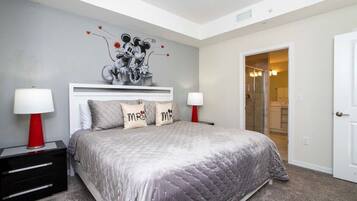 A bedroom with a large bed, two bedside tables with lamps, a white headboard, and a wall mural.