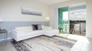 A modern living room with a white sectional sofa, a large abstract painting, and a view of a balcony with outdoor furniture.