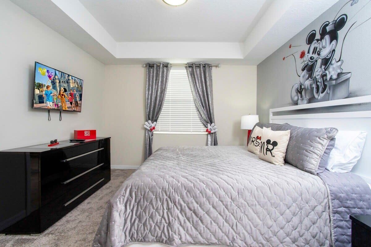A bedroom with a bed, a TV, a black entertainment unit, and a Mickey Mouse mural.