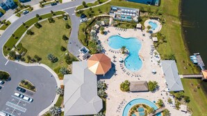An aerial view of a resort with a large central pool, multiple smaller pools, and a covered pavilion.