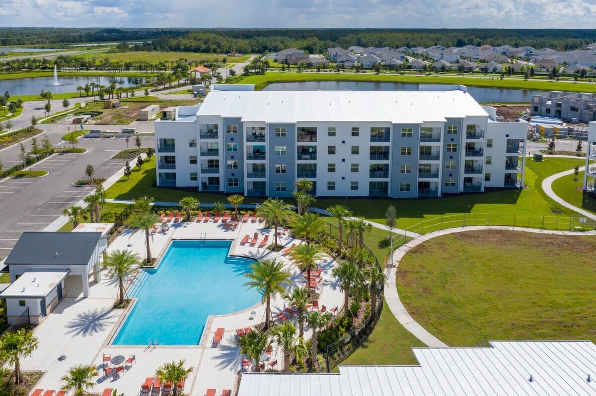 A modern hotel with a large pool, multiple balconies, and a well-maintained lawn area.