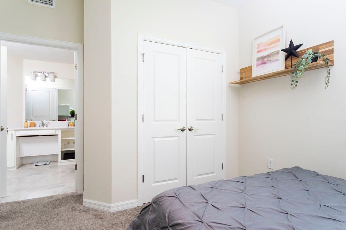 A bedroom with a bed, a white wardrobe, a mirror, and a shelf with decorative items.