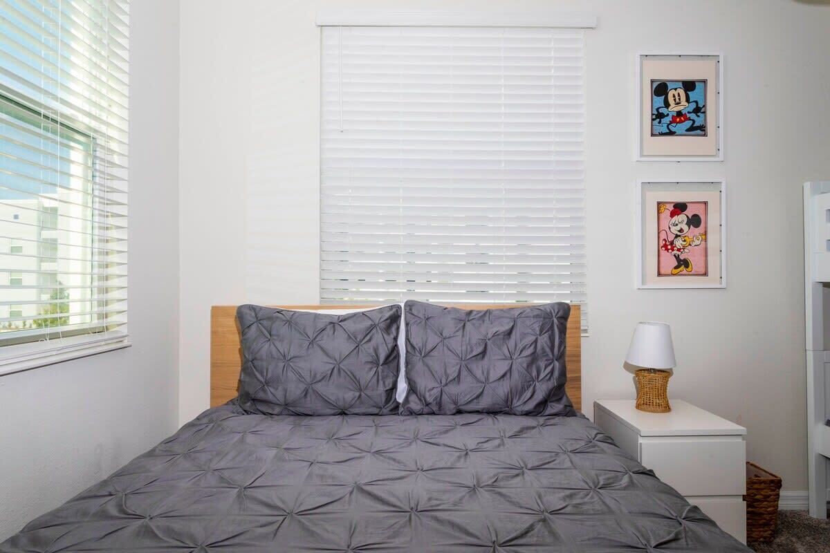 A neatly arranged bedroom with a bed, a bedside table with a lamp, and two framed pictures on the wall.