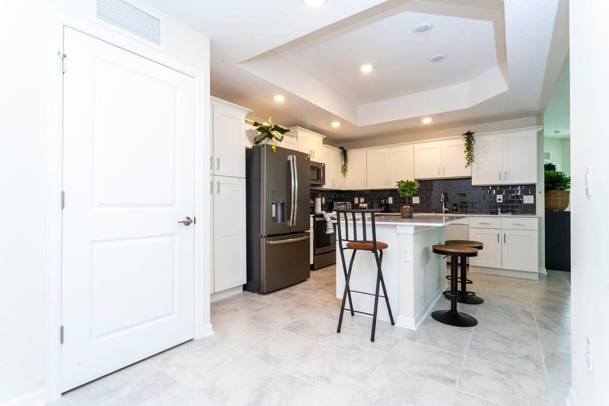 A modern kitchen with white cabinets, a black refrigerator, and a central island with stools.