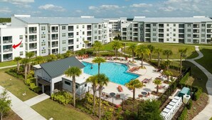 A modern hotel with a central swimming pool surrounded by palm trees and lounge chairs.