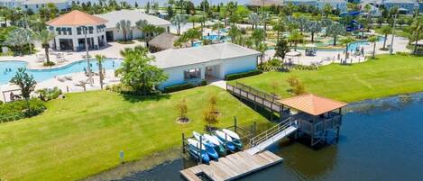 A resort with a central building, multiple swimming pools, a dock with boats, and a lake view.