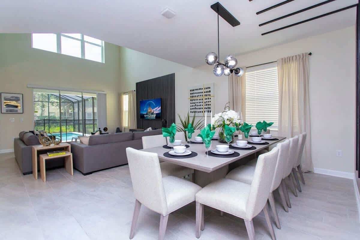 Uma sala de estar moderna com área de jantar, sofá, TV e vista para o exterior.