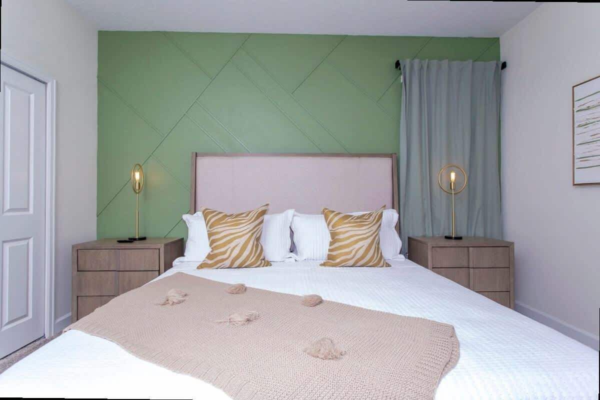 A bedroom with a bed, two bedside tables, a headboard, and a green accent wall.