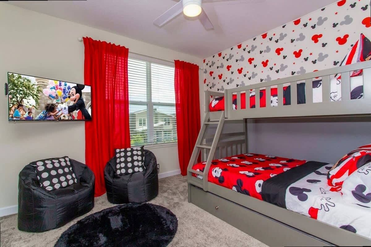 Une chambre avec un lit superposé, deux fauteuils poire, une télévision et des rideaux rouges.