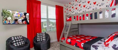 A bedroom with a bunk bed, two bean bags, a TV, and red curtains.