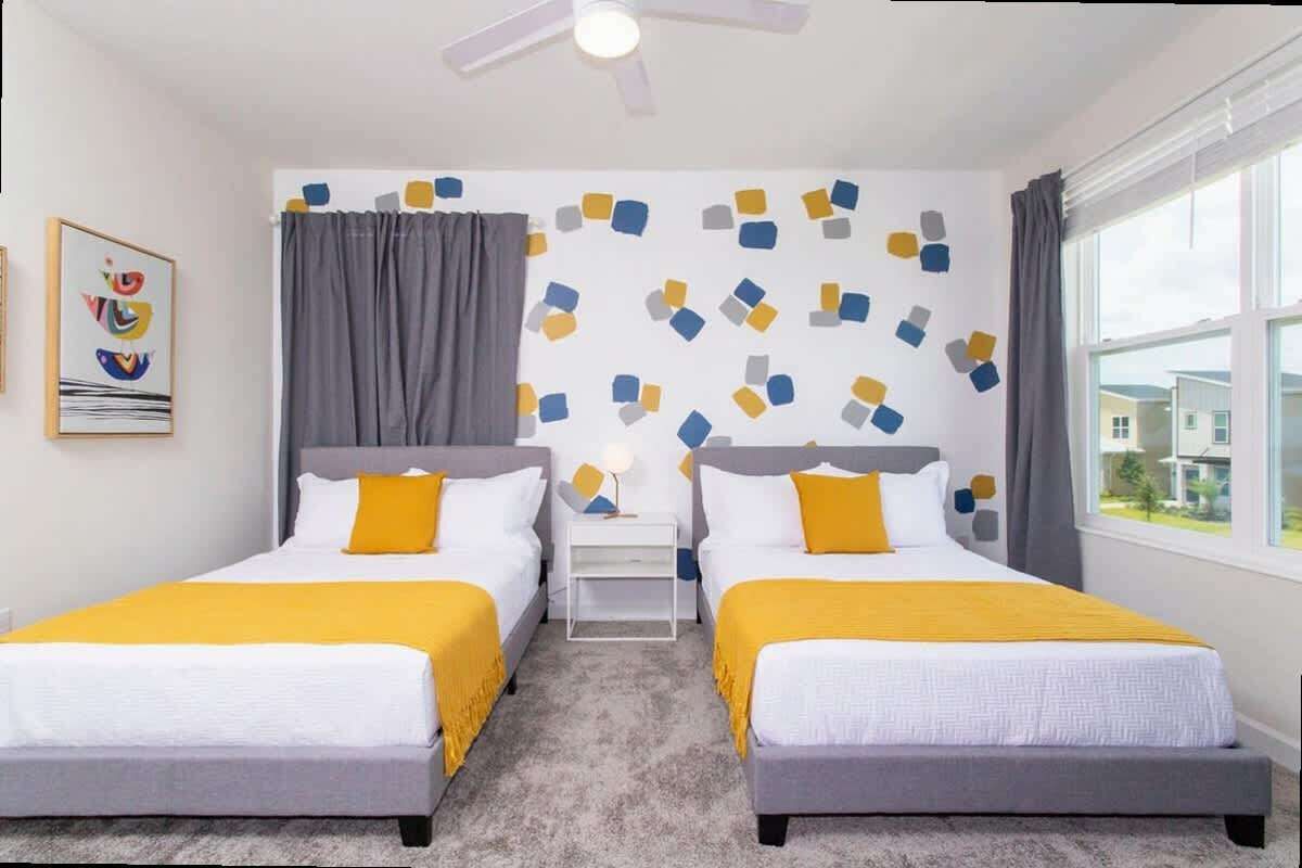 A hotel room with two beds, a ceiling fan, a window with curtains, and a wall with a geometric pattern.