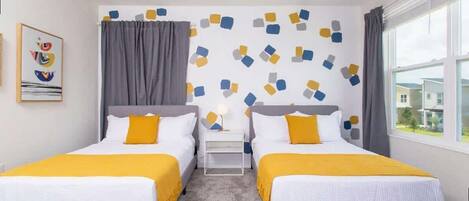 A hotel room with two beds, a ceiling fan, a window with curtains, and a wall with a geometric pattern.