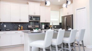 Una cocina moderna con armarios blancos, electrodomésticos de acero inoxidable y una zona de bar con sillas blancas.