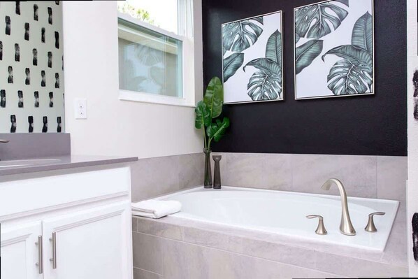 A modern bathroom with a bathtub, white cabinetry, and a window with a view. - Gorgeous Family Friendly 5 Bd w/ Pool Close to Disney @ Storey Lake 2767 (Kissimmee)