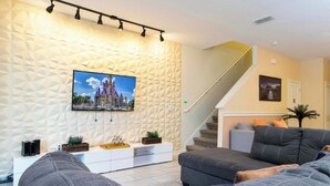 Ein modernes Wohnzimmer mit Wand in geometrischem Muster, einem Flachbildfernseher, einer Treppe und einem Sofa.