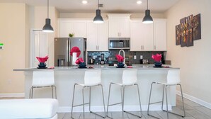 A modern kitchen with white cabinets, a central island with bar stools, a refrigerator, and a microwave.