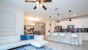 A modern living room with a white sofa, blue rug, and a kitchen area with white cabinets and a microwave.