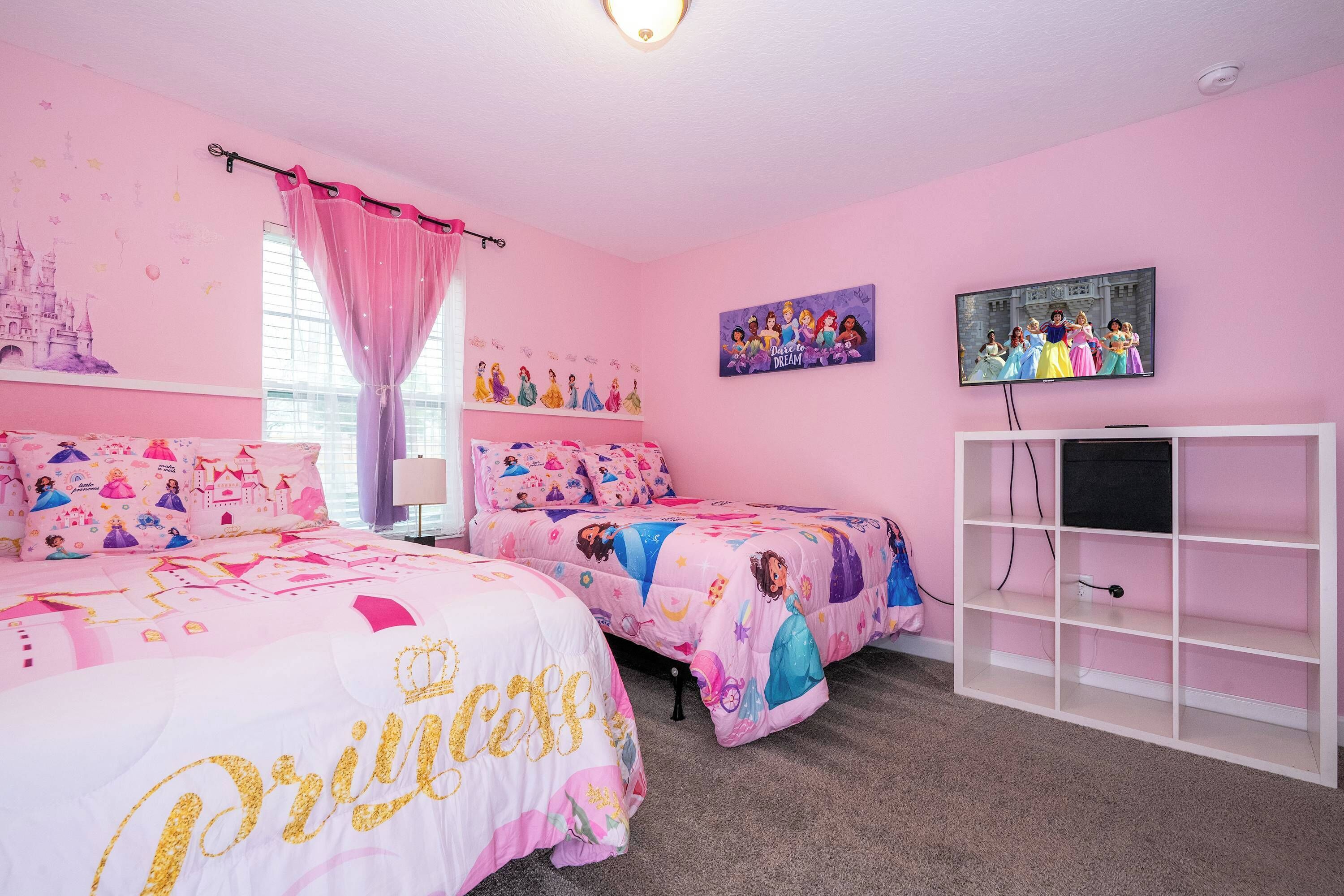 Un dormitorio con temática rosa, con dos camas, un televisor y un estante blanco.