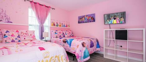 Un dormitorio con temática rosa, con dos camas, un televisor y un estante blanco.