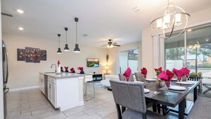 A modern kitchen with white cabinets, a central island, pendant lighting, and a dining area with a dark table and chairs.