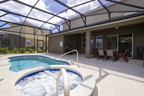 Piscina externa com hidromassagem, cercada por um espaço coberto com área de estar e mesas.
