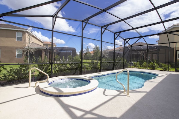 An indoor swimming pool with a hot tub, surrounded by a glass enclosure, and houses visible in the background.
