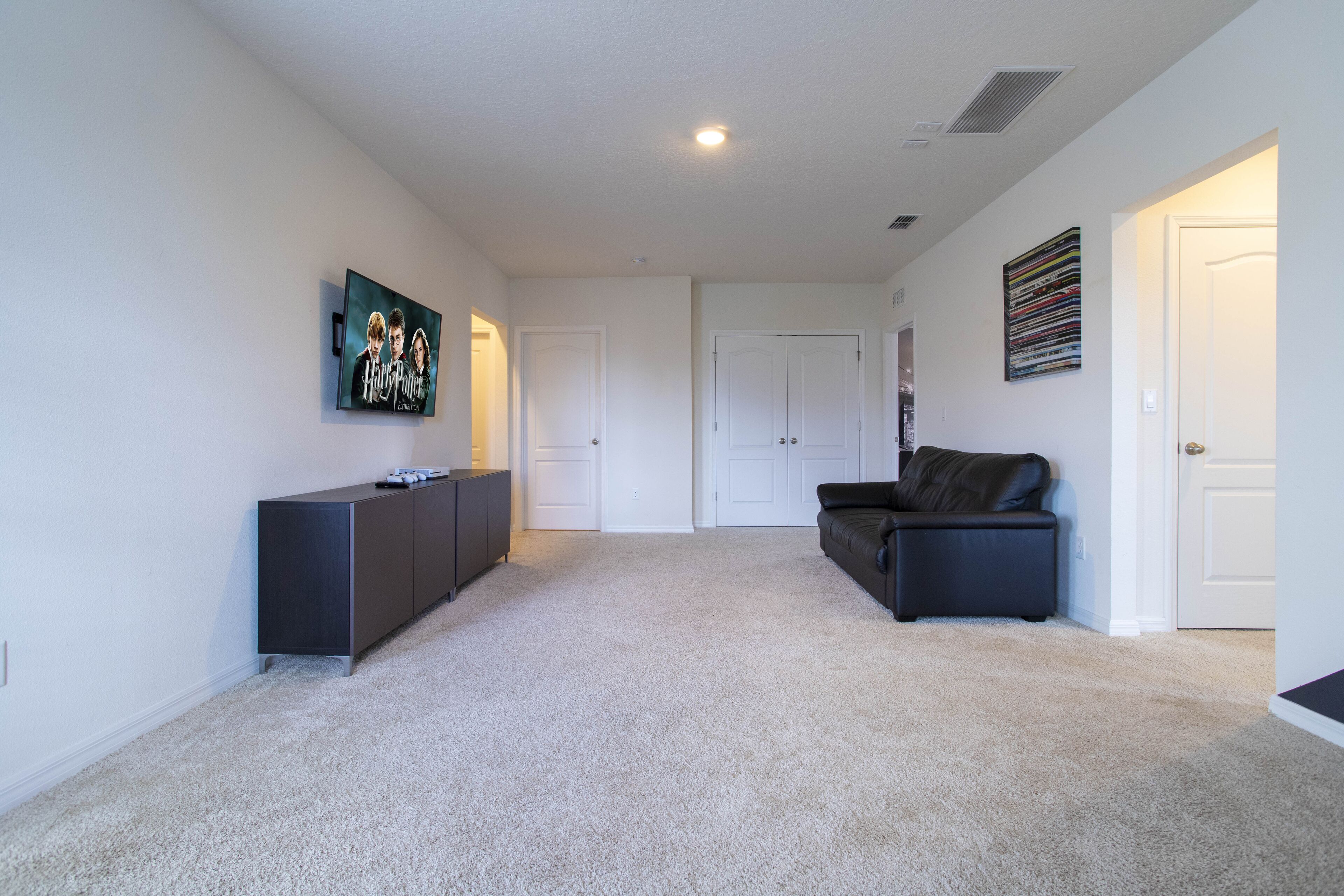 A spacious living room with a dark-colored sofa, a flat-screen TV mounted on the wall, and a dark-colored cabinet.