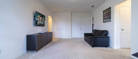 A spacious living room with a dark-colored sofa, a flat-screen TV mounted on the wall, and a dark-colored cabinet.