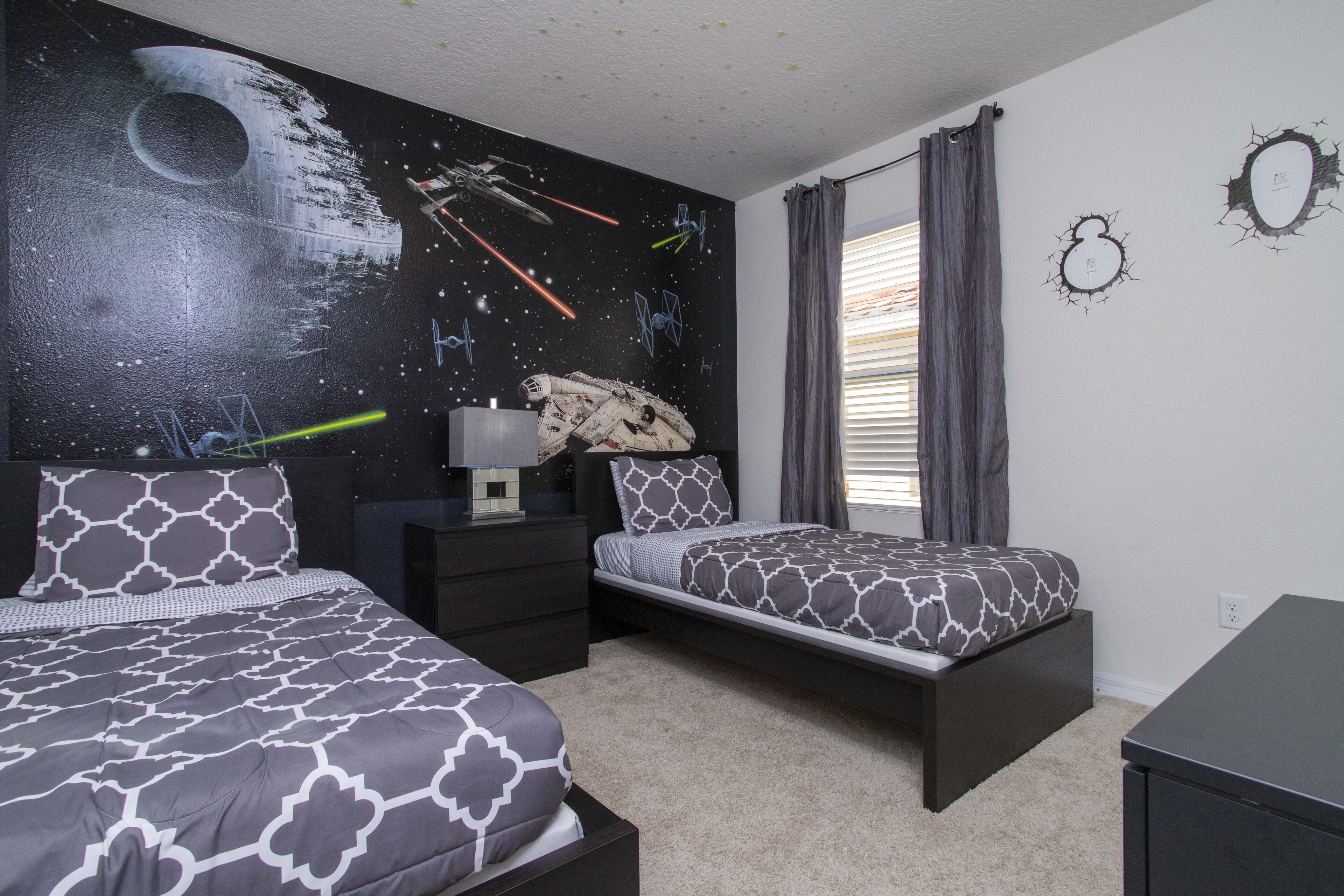 A bedroom with two beds, a Star Wars themed wall, and a window with curtains.